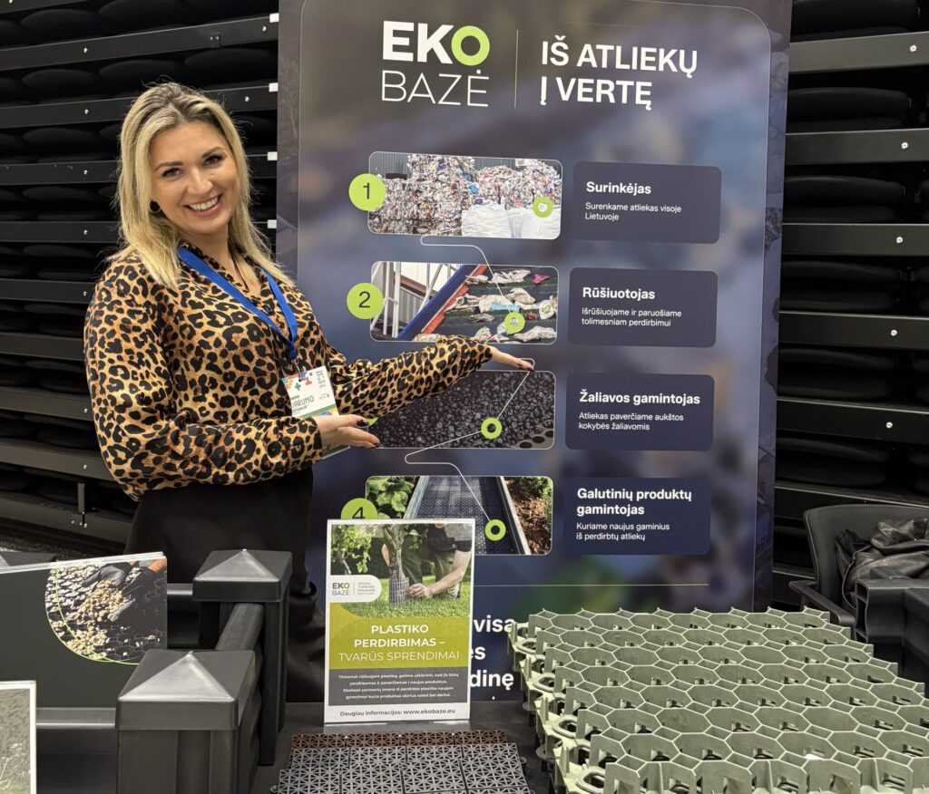 Ekobazė kolegė stovi prie stendo ir rodo į gaminius pagamintus iš perdirbto plastiko. Jaunimo tvarumo festivalis 2926 Litexpo